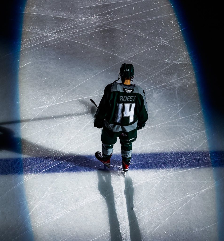 Everett Silvertips forward Austin Roest stands on the blue line, in a spotlight, with his back to the camera.