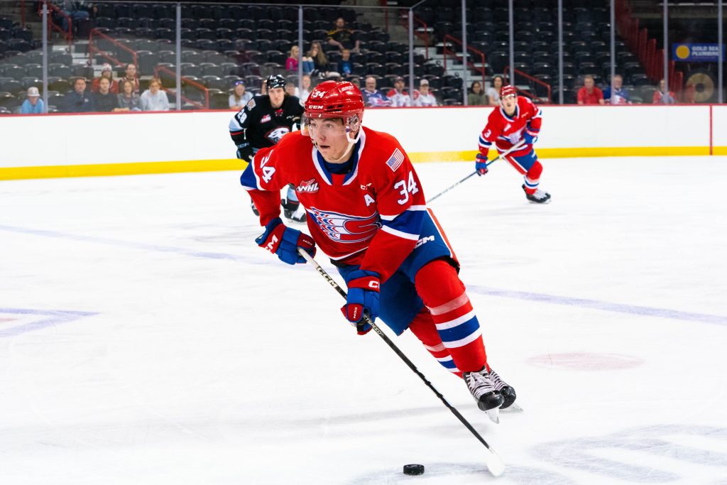 An action shot of Conner Roulette on the ice. He's in the red Chiefs uniform, skating with the puck.