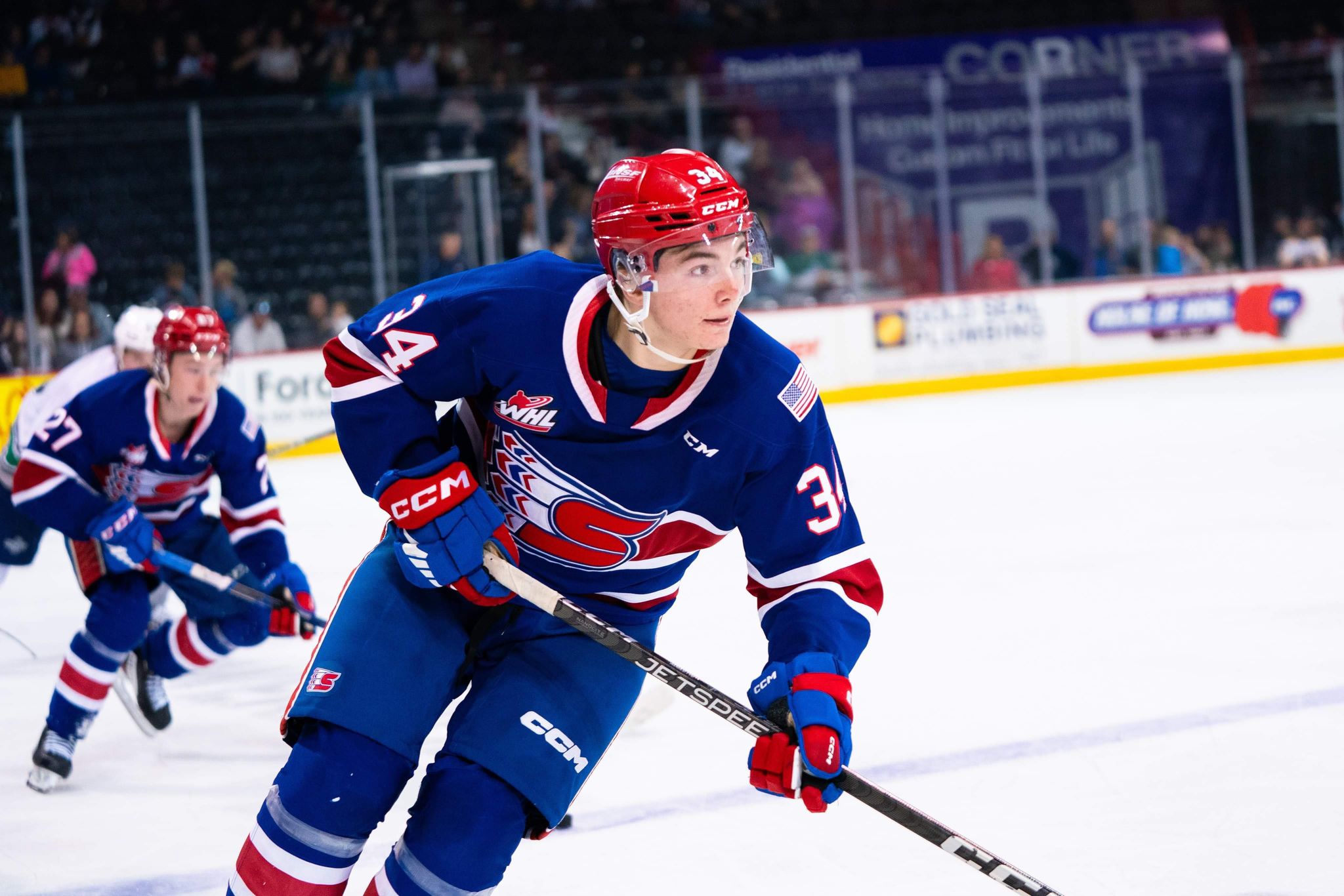 An action shot of Conner Roulette on the ice in the blue Chiefs uniform. He's skating, holding his stick, looking to the right.