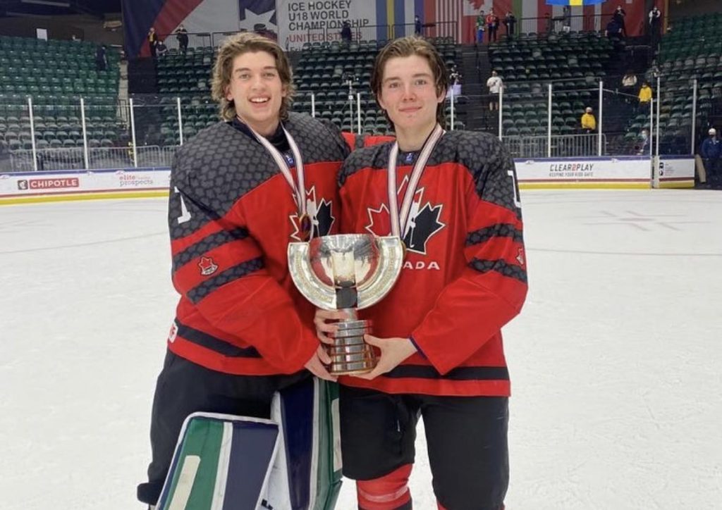 Thomas Milic and Conner Roulette pose for a photo with the first place trophy. They're both wearing Team Canada jerseys with gold medals around their neck.