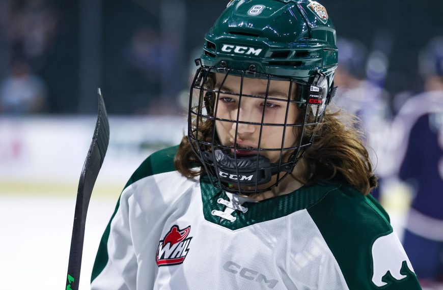 Silvertips player Ethan Makokis in the white jersey. He has a green helmet on and a black face cage on.