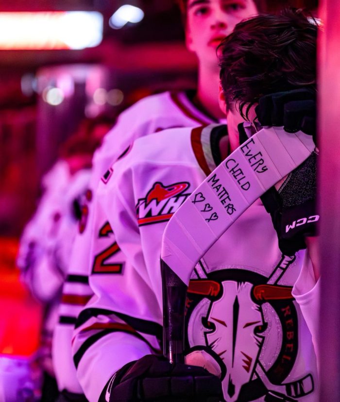 Dwayne Jean Jr. stands on the bench with his head down. On his stick are the words "every child matters."