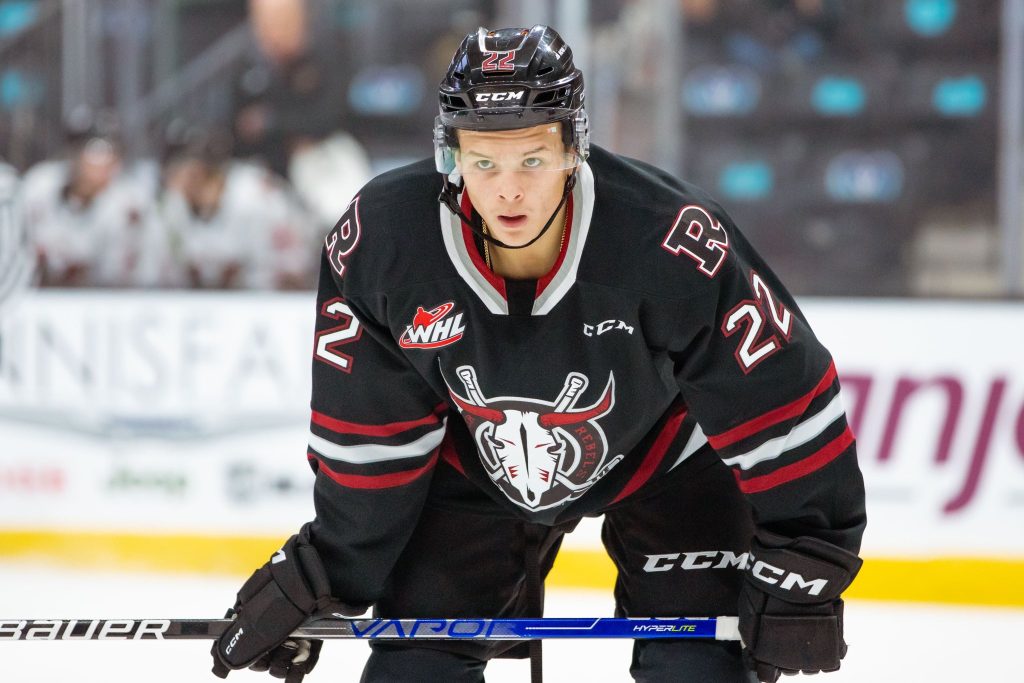 Red Deer Rebels forward Dwayne Jean Jr. in the Rebels’ black jersey. He’s on the ice, leaning over with his stick in his hands.