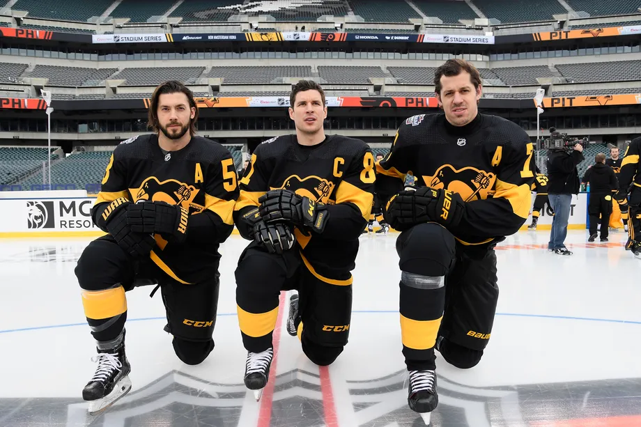 Kris Letang, Sidney Crosby, and Evgeni Malkin kneel on the ice in their black Penguins uniforms